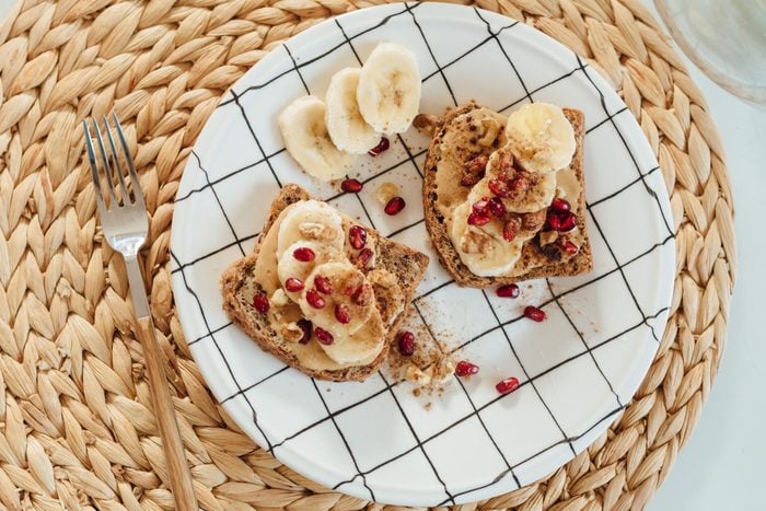 Shot of the peanut butter toast with banana slices and pomegranate on a plate.