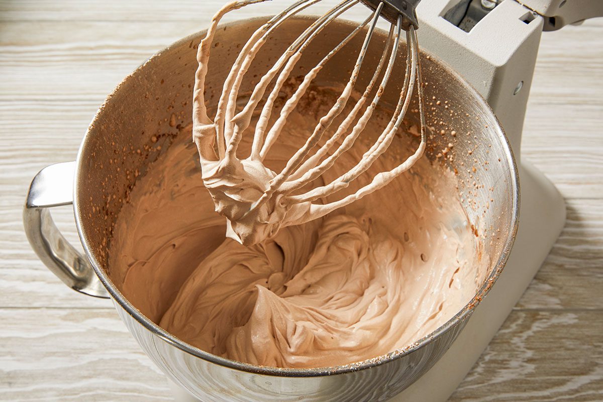 Top-down image of a whipped topping being mixed in a stand mixer bowl, preparing the final topping for the Irish cream poke cake.