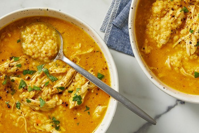 Overhead image of a spoon lifting a portion of Italian Penicillin Soup from a bowl, highlighting shredded chicken, pastina, and creamy broth. This final step emphasizes warmth, comfort, and ready-to-eat appeal.