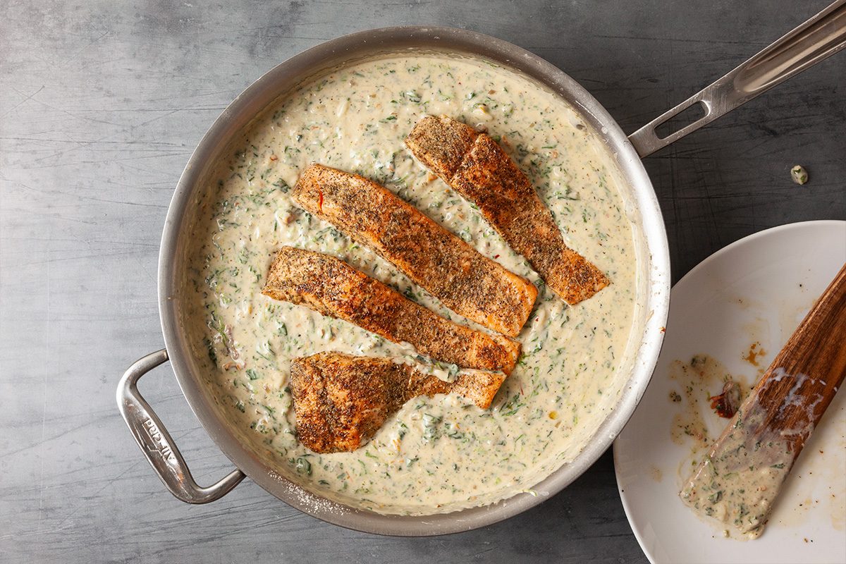 Overhead view of salmon fillets placed back into the creamy spinach sauce in the skillet. The fish rests partially submerged as it finishes cooking.