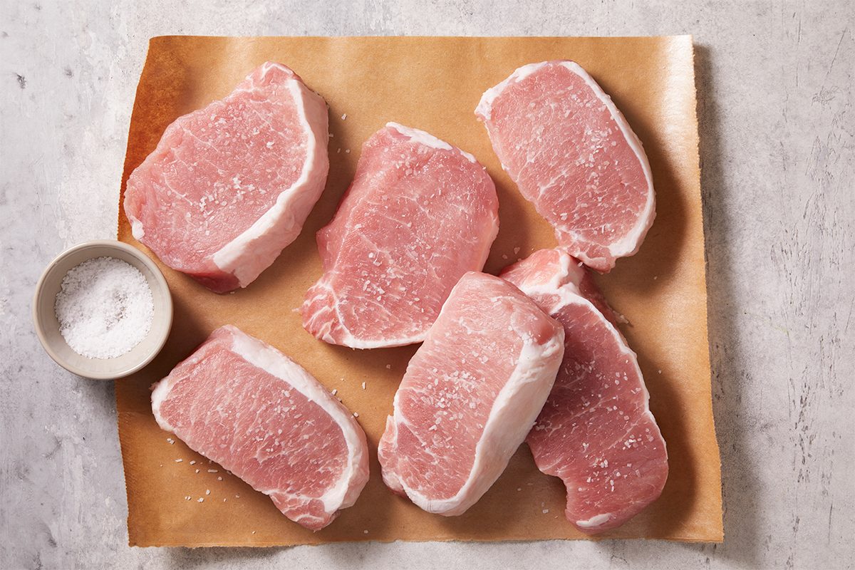 Overhead step-by-step food photography showing raw boneless pork loin chops arranged on parchment paper in preparation for Dijon Pork Chops.