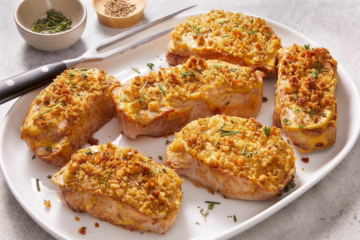 Overhead food photography showing Dijon Pork Chops served family-style on a white platter with a crisp bread crumb crust.