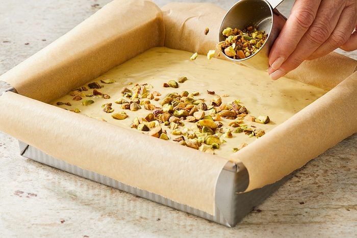 sprinkling cheesecake filling in pan with pistachios