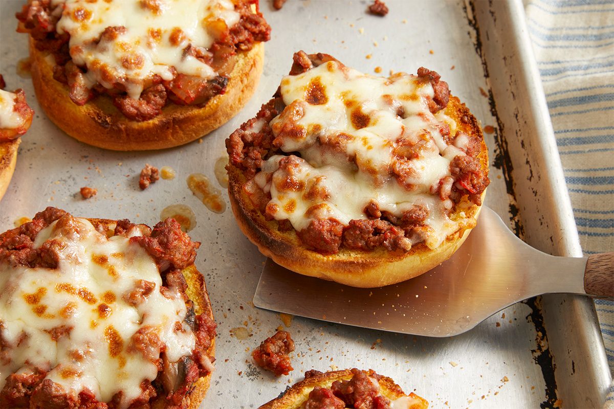 Overhead, horizontal close-up of baked open-faced pizza burgers with melted mozzarella cheese. The cheese is lightly browned and bubbly over the beef mixture, showing the finished cooking stage before serving.