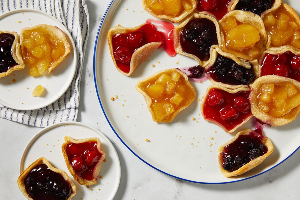 Overhead Push and Pulls image of the baked Pull-Apart Pie partially separated, with several mini pie sections removed and placed on small plates. The image emphasizes the interactive, shareable nature of the dessert and the variety of fruit fillings.