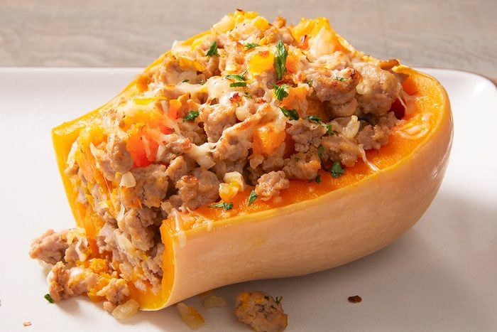 A halved butternut squash filled with a mixture of ground meat, vegetables, and melted cheese, garnished with chopped herbs, served on a white plate.
