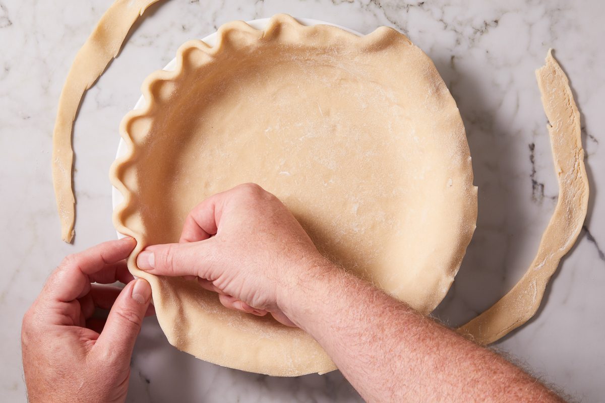 fluting edges of pie dough inside pie pan