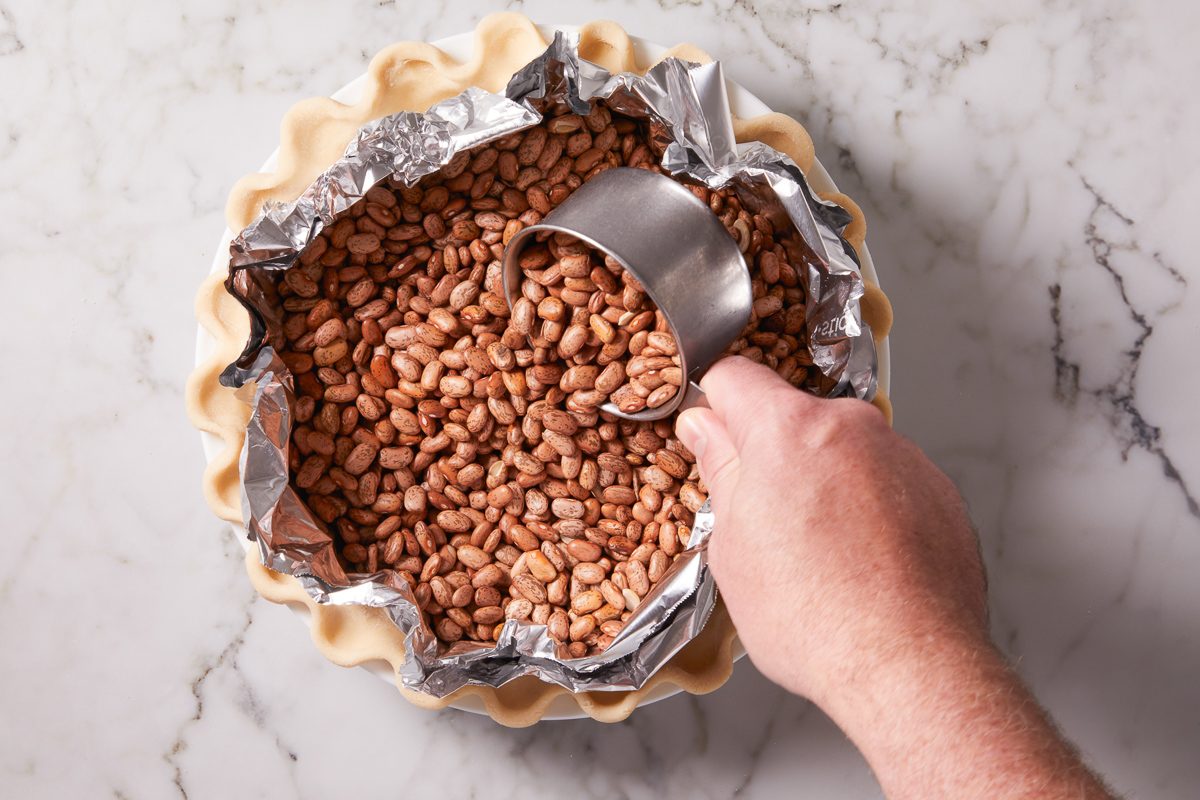 adding dried beans to pie crust lined with foil