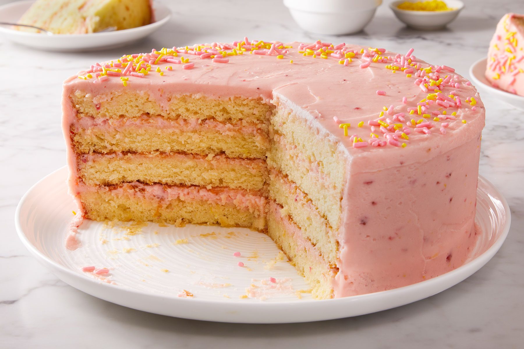 Strawberry Lemonade Cake with a big piece cut out of it. Placed on a white serving plate.