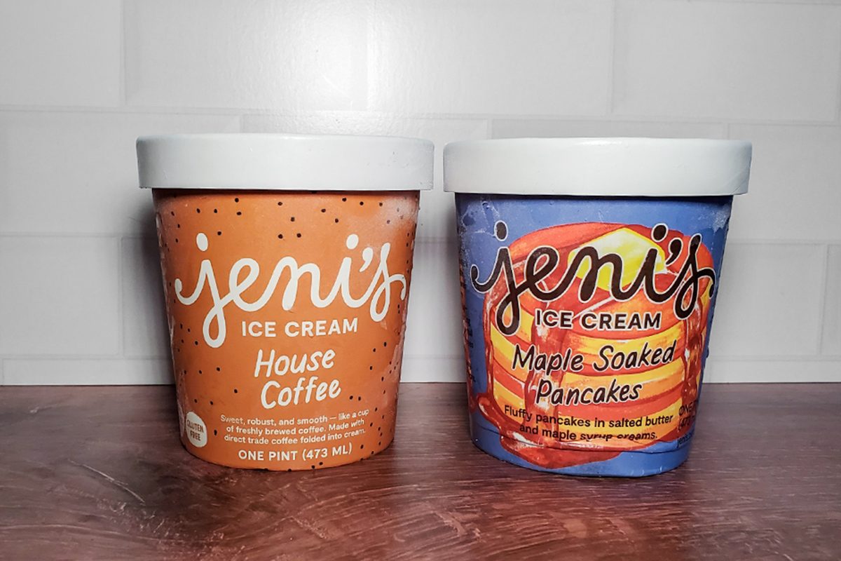 Two pints of Jeni’s ice cream sit side by side on a wooden surface. The left pint is House Coffee flavor in a brown container; the right is Maple Soaked Pancakes flavor in a purple and orange container.