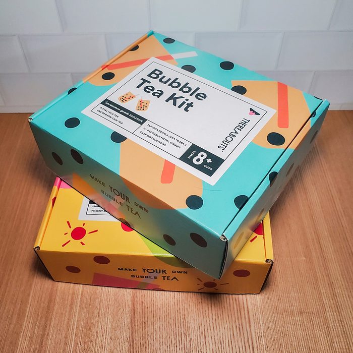 Two colorful boxes on a wooden surface. The top box is teal with black dots, labeled 
