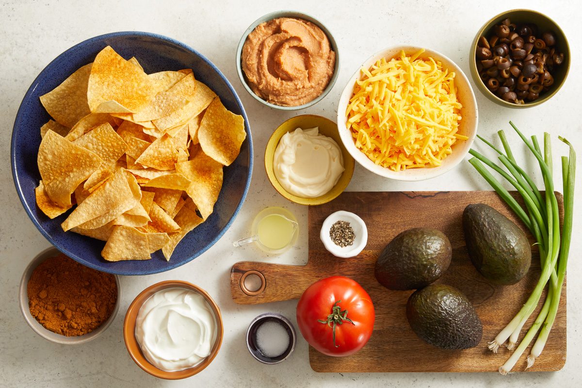 bean dip, avocados, lemon juice, sour cream, mayonnaise, taco seasoning, shredded cheese, olives, green onions, tomatoes and tortilla chips