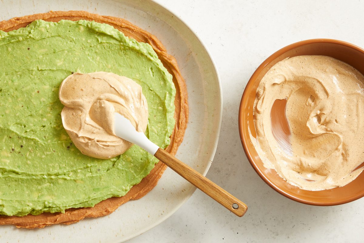sour cream, mayonnaise and taco seasoning mixture being spread over avocado layer