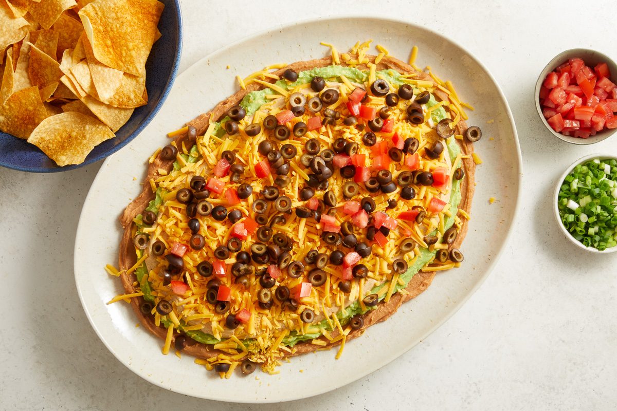 dip layers topped with shredded cheese, sliced olives, green onions, and chopped tomato