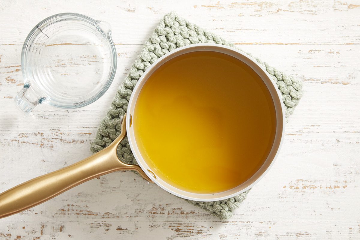 Overhead shot of melted butter in a saucepan with a potholder underneath, placed on a white wooden surface.
