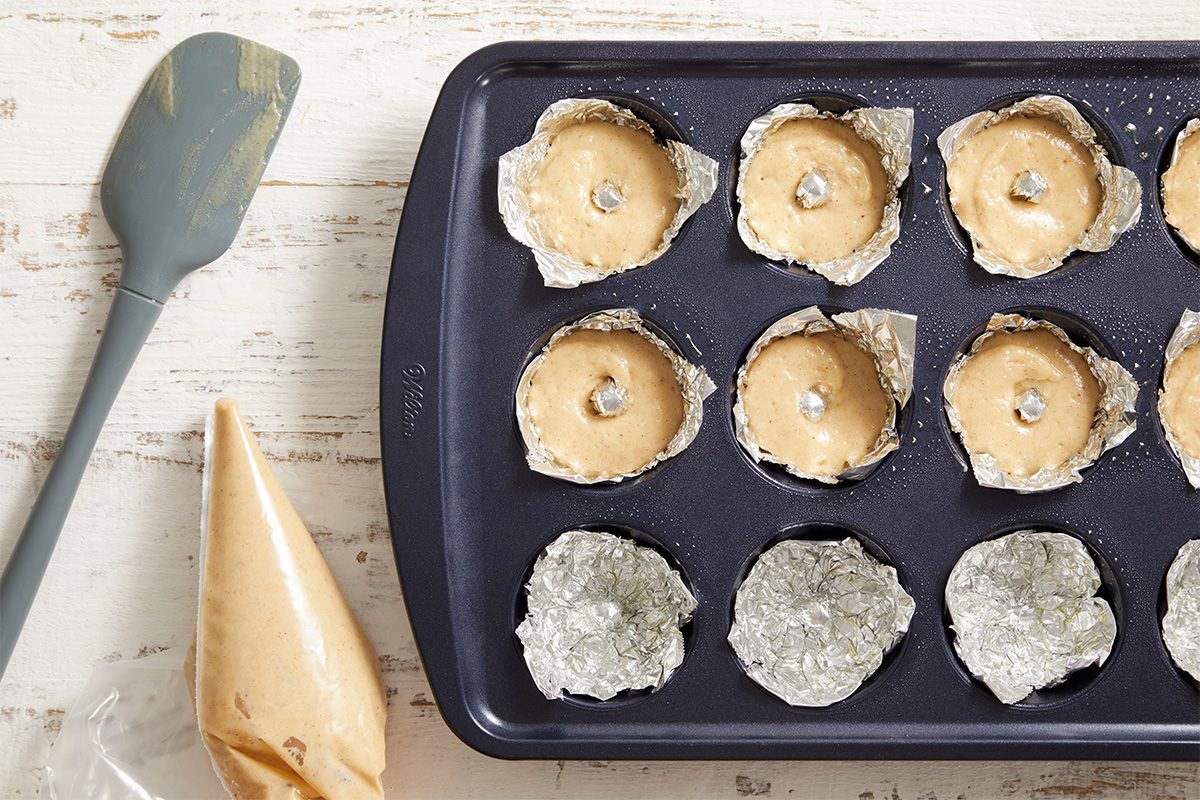 Overhead shot of doughnut batter piped into the foil molds in a muffin tray, ready for baking.