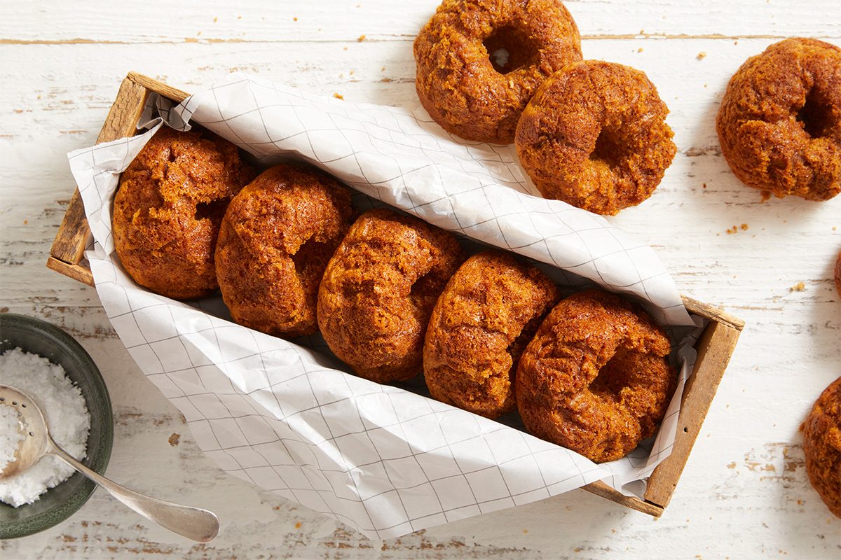 Overhead shot of freshly Baked Doughnuts arranged in a wooden tray lined with parchment paper, a small bowl of sugar on the side.
