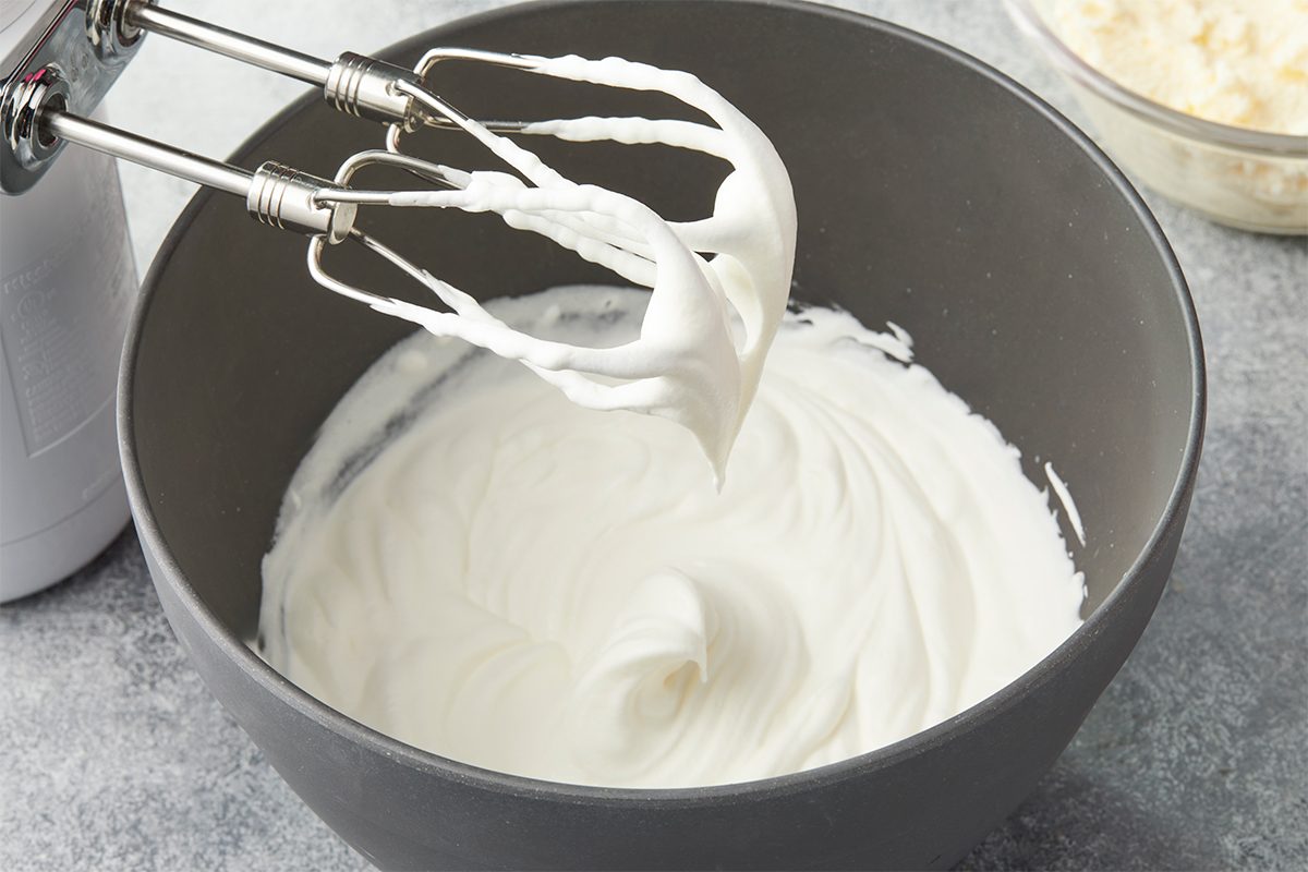 In a large bowl, beat cream and remaining 2 tablespoons sugar until soft peaks form; fold in remaining tub of mascarpone. Overhead premium image of heavy whipping cream being whipped to soft peaks in a stand mixer for incorporation into the tiramisu filling.