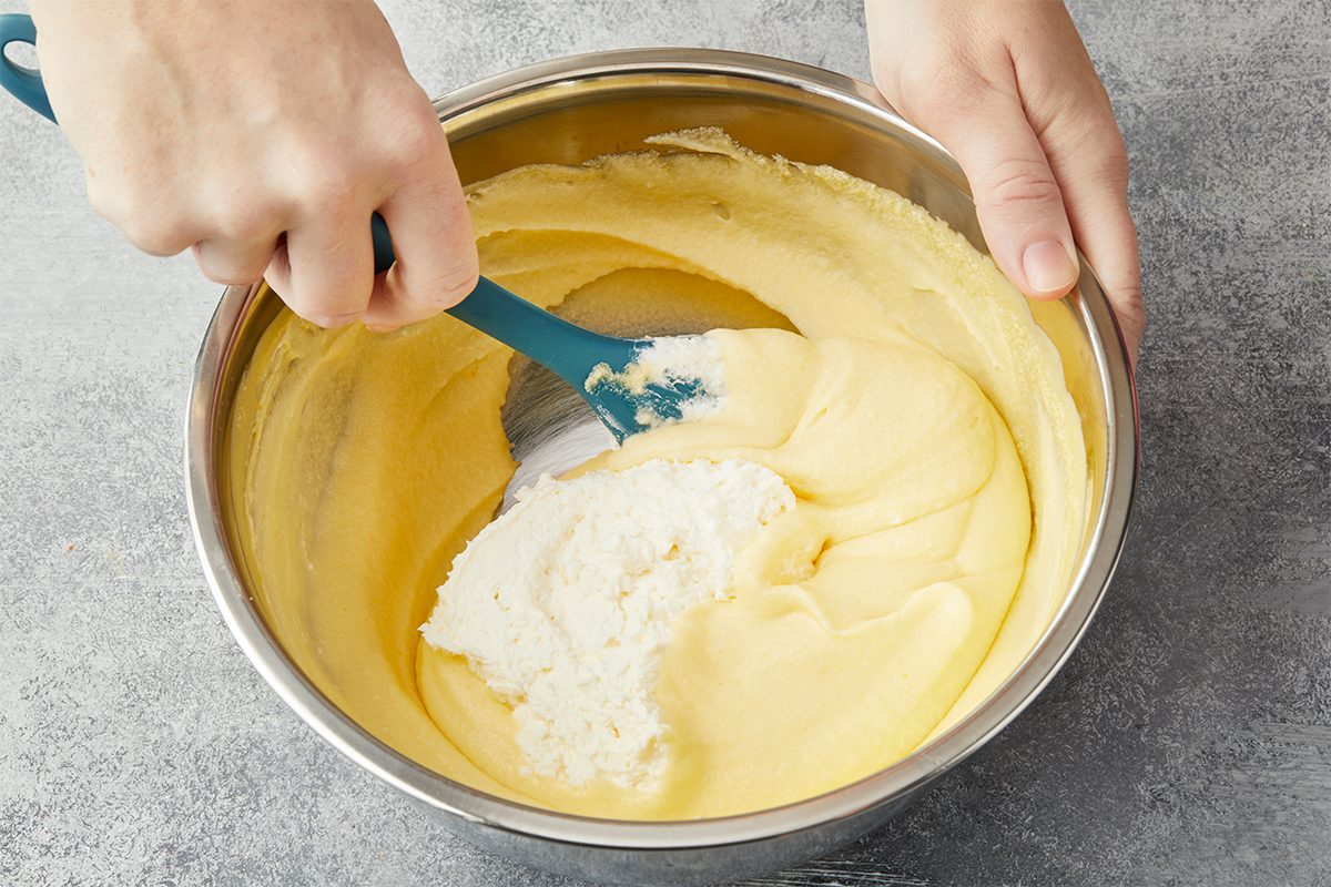 Let stand 15 minutes. Fold cream and egg mixtures together until smooth. Overhead view of whipped cream being gently folded into the mascarpone custard mixture to create a light and fluffy tiramisu filling.