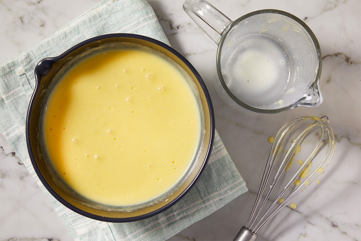 Overhead horizontal image of prepared vanilla pudding mixture with whisk and milk nearby.