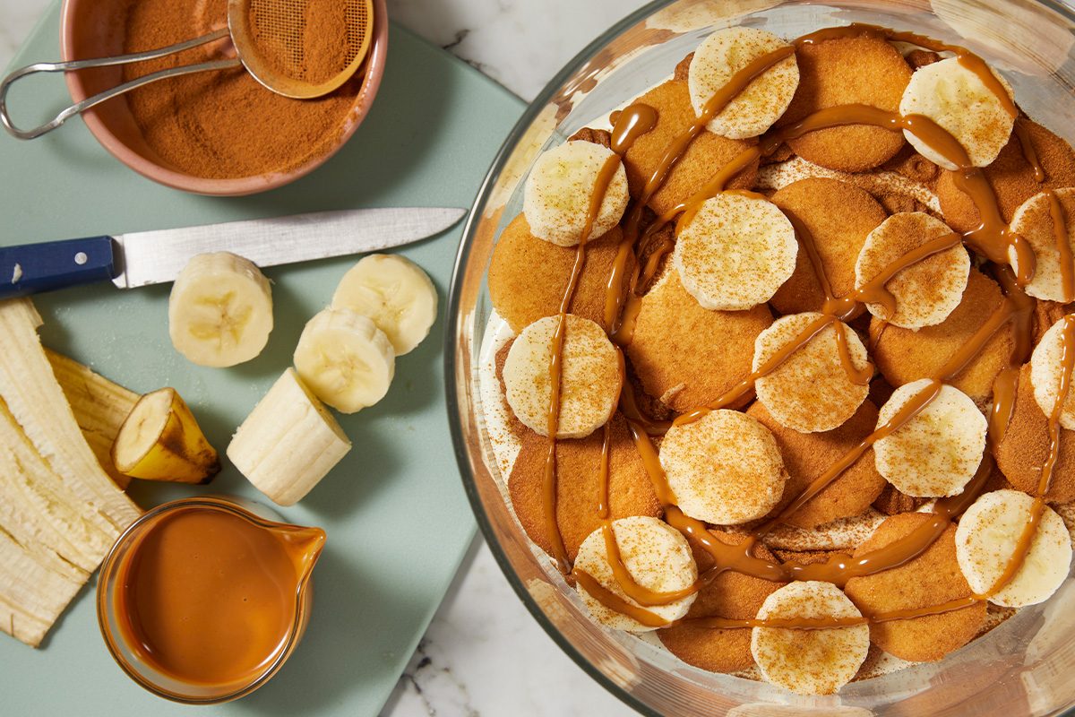 Overhead horizontal image of banana slices and cookies layered with pudding in a glass dish.