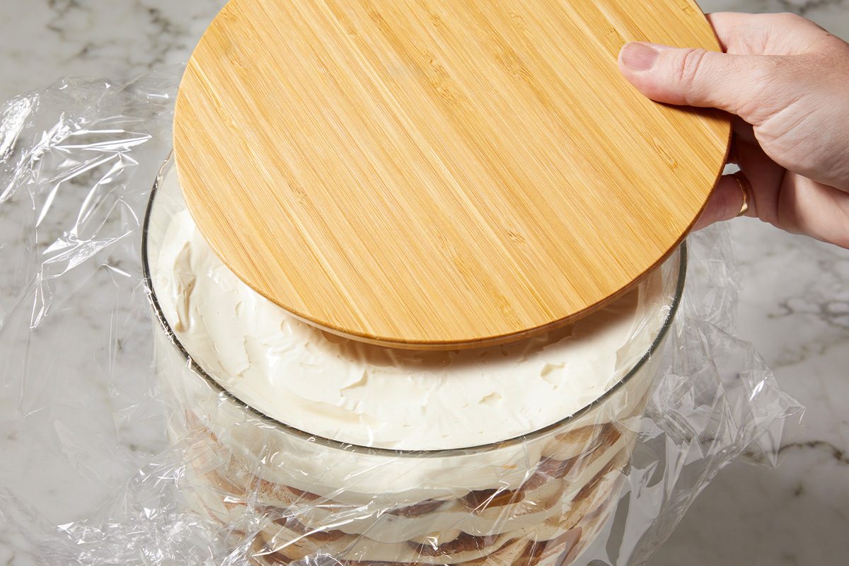 Overhead horizontal image of assembled pudding being covered and chilled in a glass container.