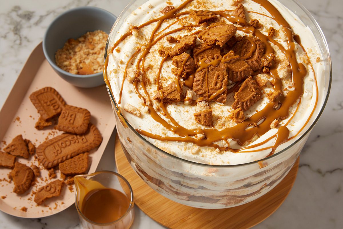 Eye-level horizontal image of finished Biscoff banana pudding topped with cookie crumbles and drizzle.
