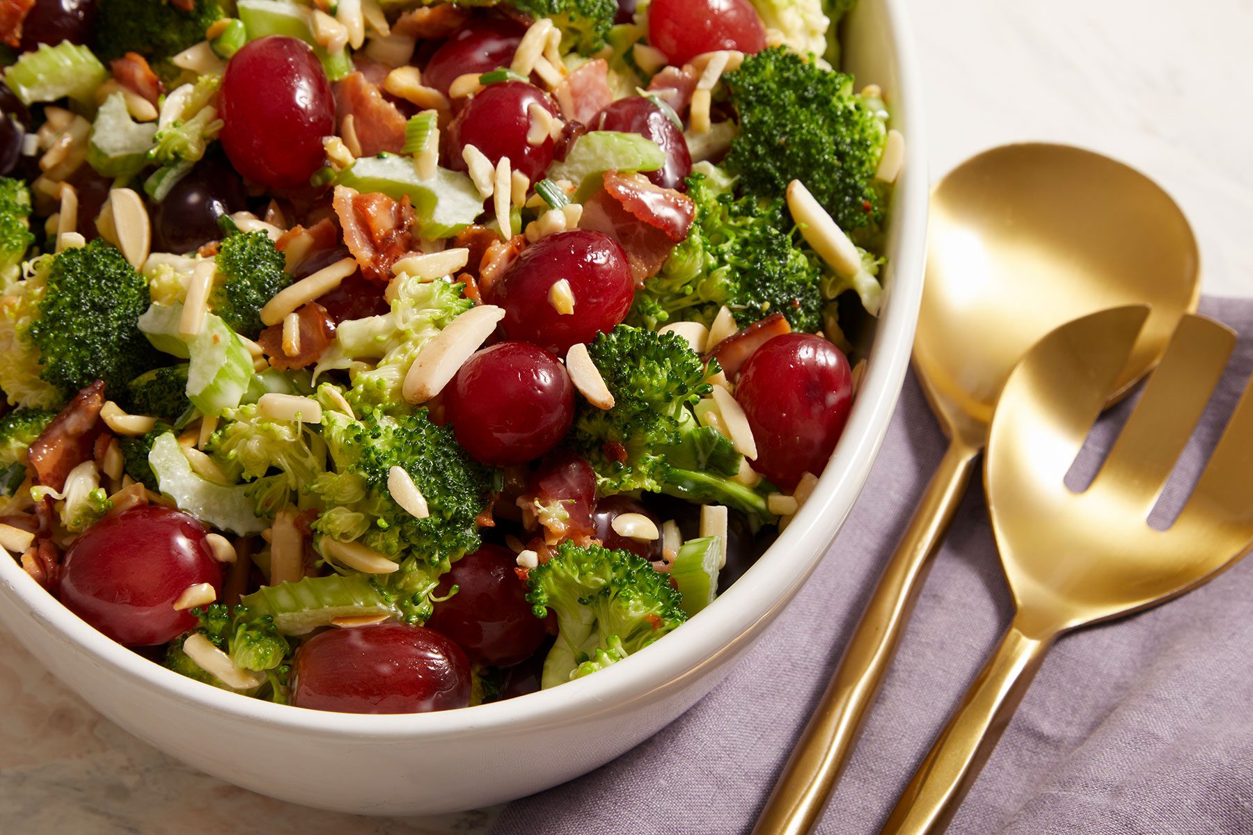 Broccoli Grape Salad in a white bowl with golden colored cutlery placed on side.