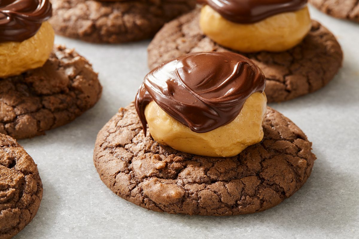 Chocolate cookies topped with a dollop of peanut butter and drizzled with melted chocolate, arranged on parchment paper.