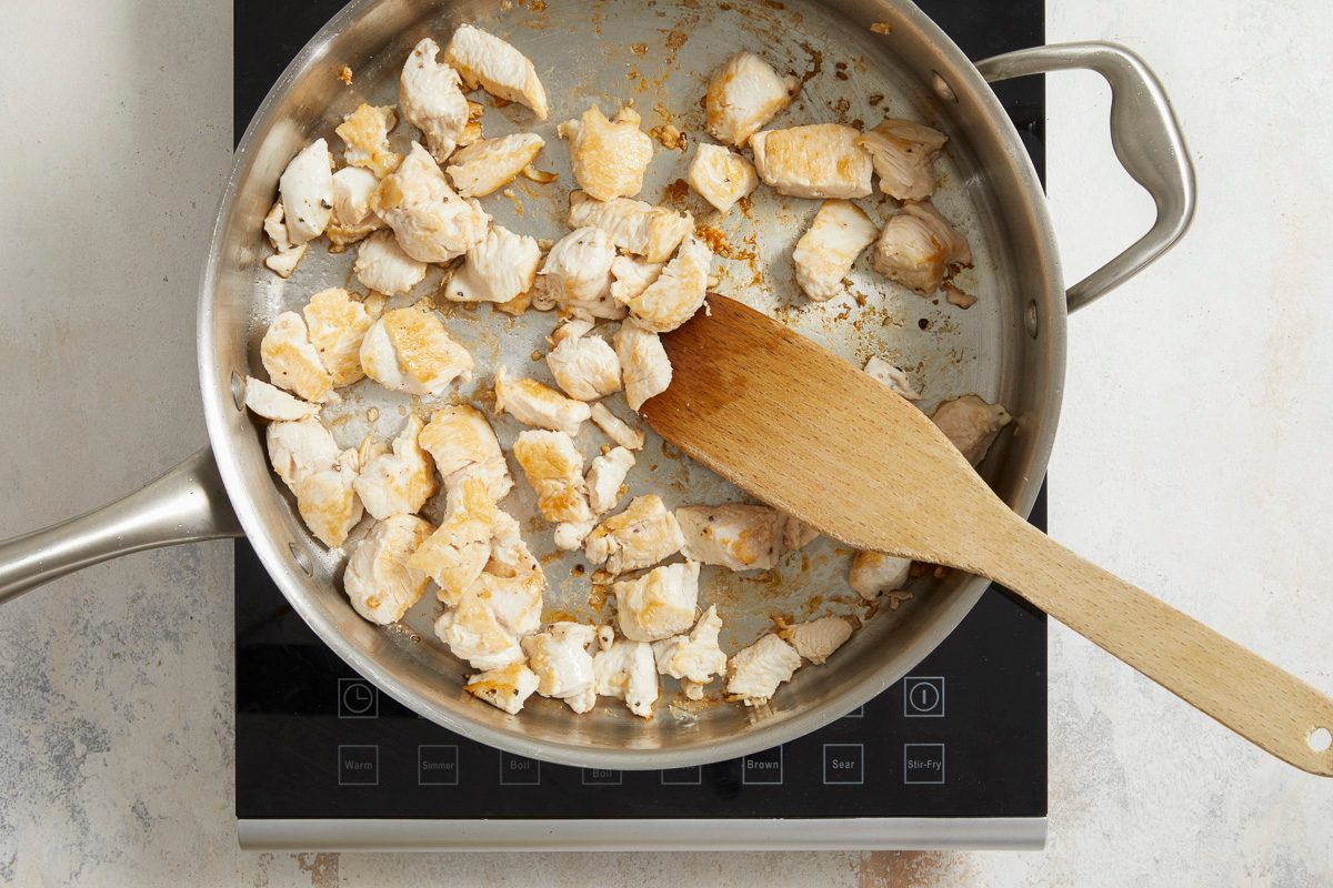 chicken being sautéed with salt and pepper in a large skillet