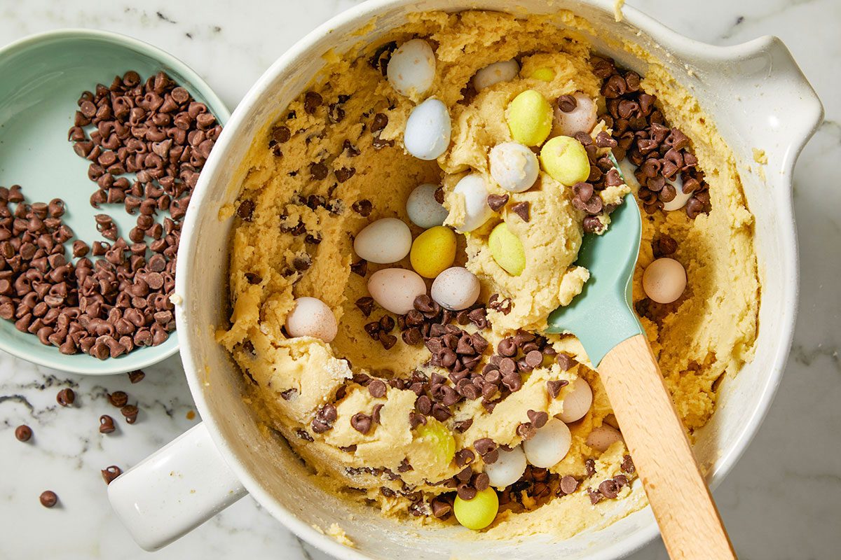 Overhead horizontal image of cookie dough with Cadbury mini eggs and chocolate chips being folded into the mixture.