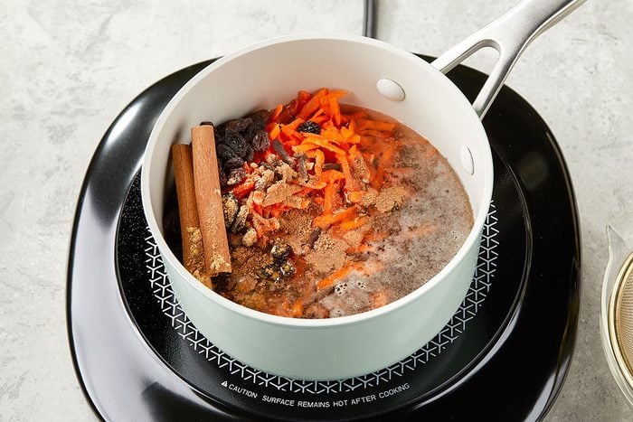 Overhead image of shredded carrots, raisins and spices simmering in a saucepan to create carrot cake syrup for a Carrot Cake White Russian cocktail.