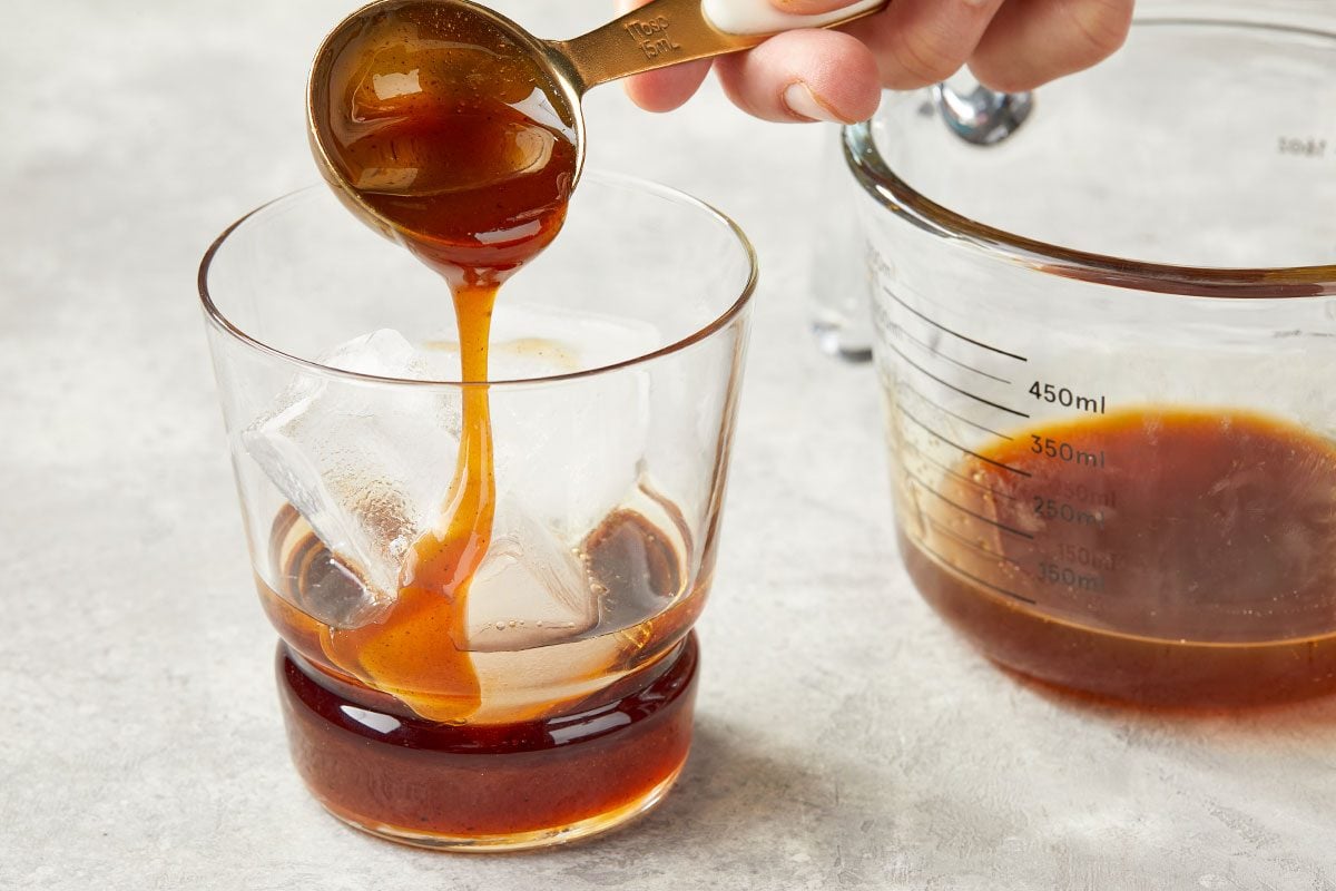 Overhead image of carrot cake syrup being poured into a glass to form the base layer of the Carrot Cake White Russian cocktail.