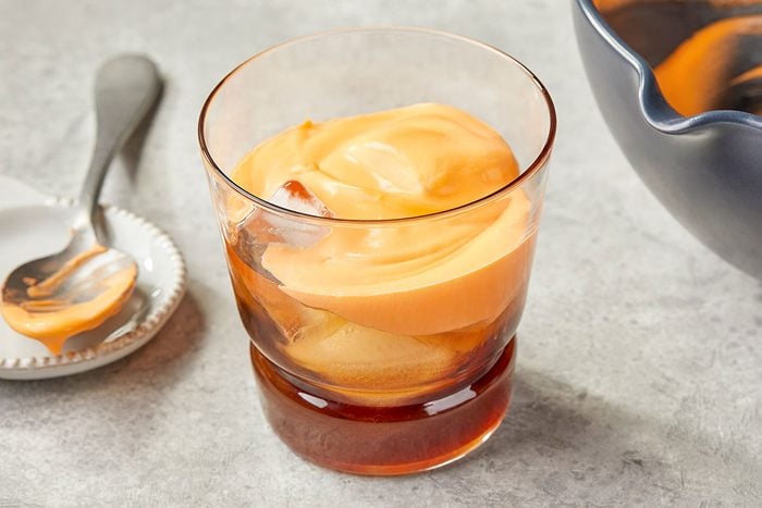 Overhead image of carrot cream being spooned into a glass layered with carrot cake syrup to assemble the Carrot Cake White Russian cocktail.
