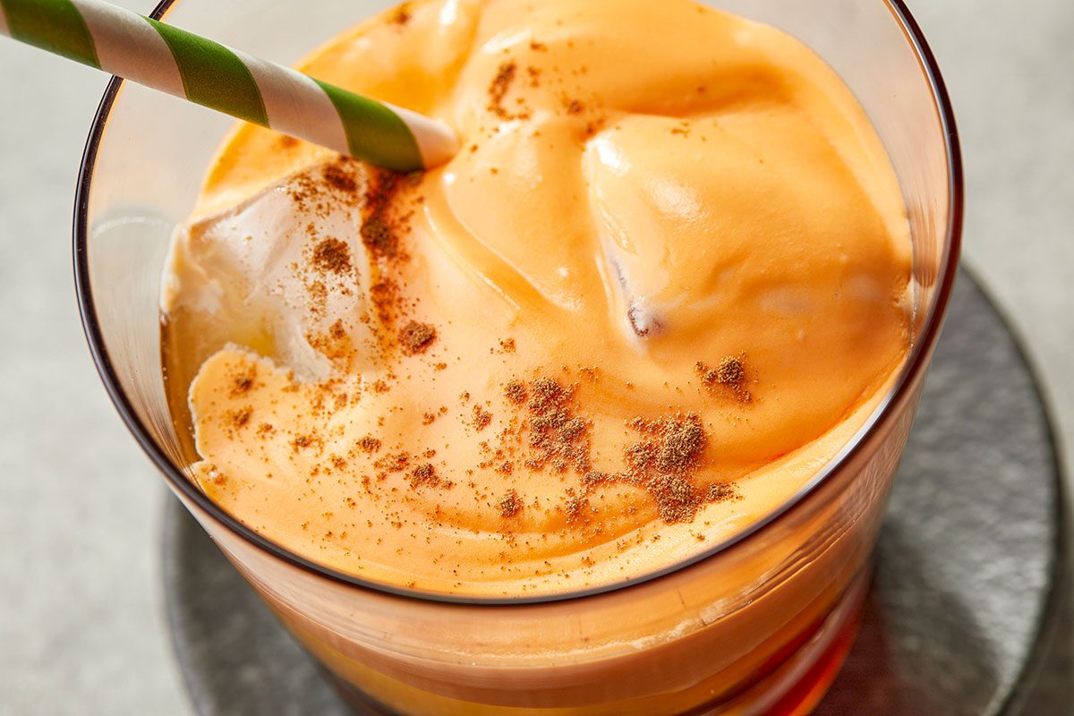 Overhead close up image of Carrot Cake White Russian cocktail served in a glass with creamy carrot topping and sprinkled cinnamon.