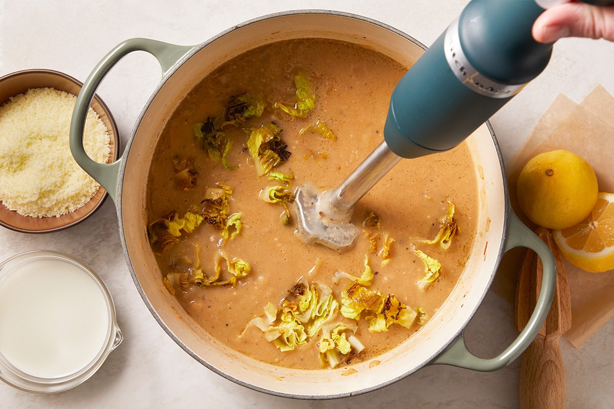 Overhead horizontal image of soup being blended with an immersion blender to create a creamy base.