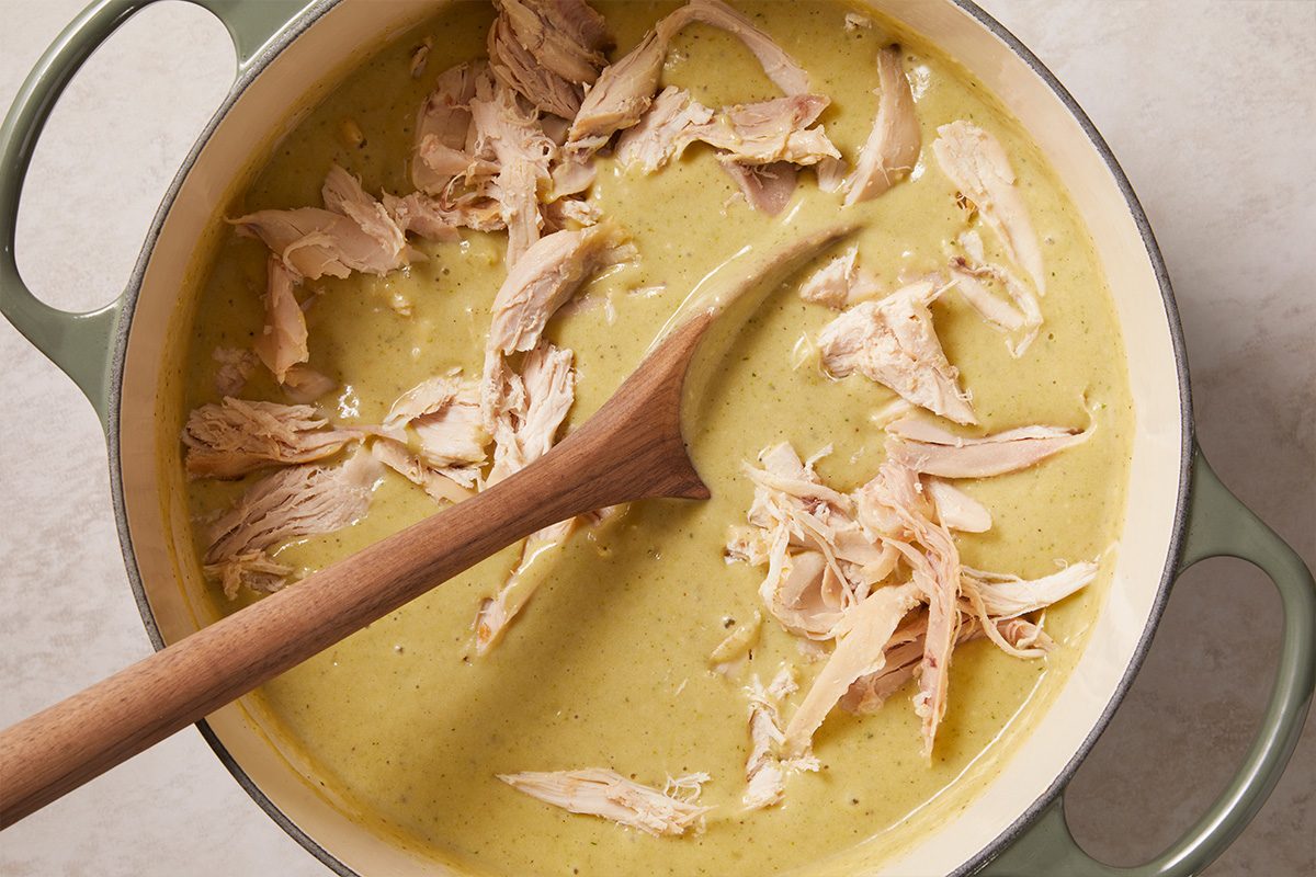 Overhead horizontal image of shredded rotisserie chicken being added to creamy soup.