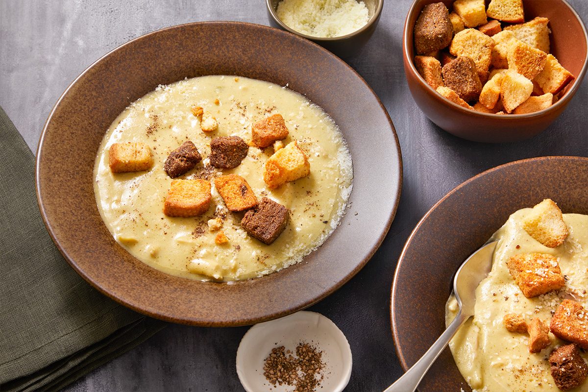 Overhead horizontal image of multiple bowls of Chicken Caesar soup served with croutons and cheese.
