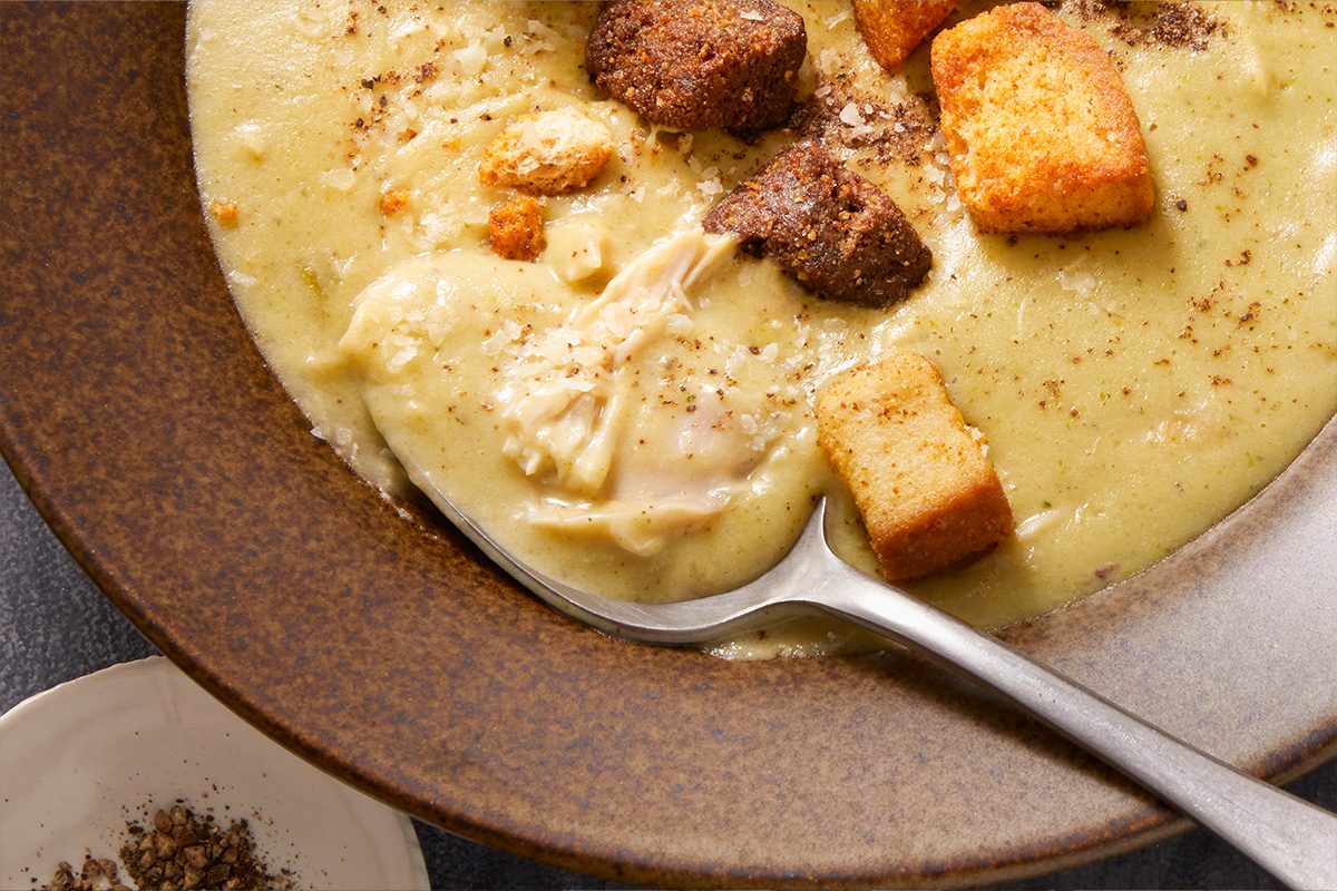 Overhead horizontal close-up of Chicken Caesar soup highlighting creamy texture, chicken, and croutons.