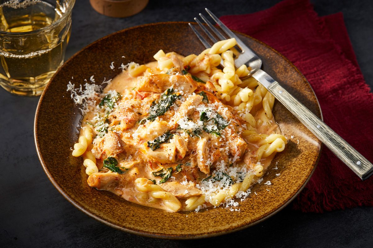 Overhead horizontal image of a plated serving of chicken Parma rosa over pasta with grated Parmesan and herbs.