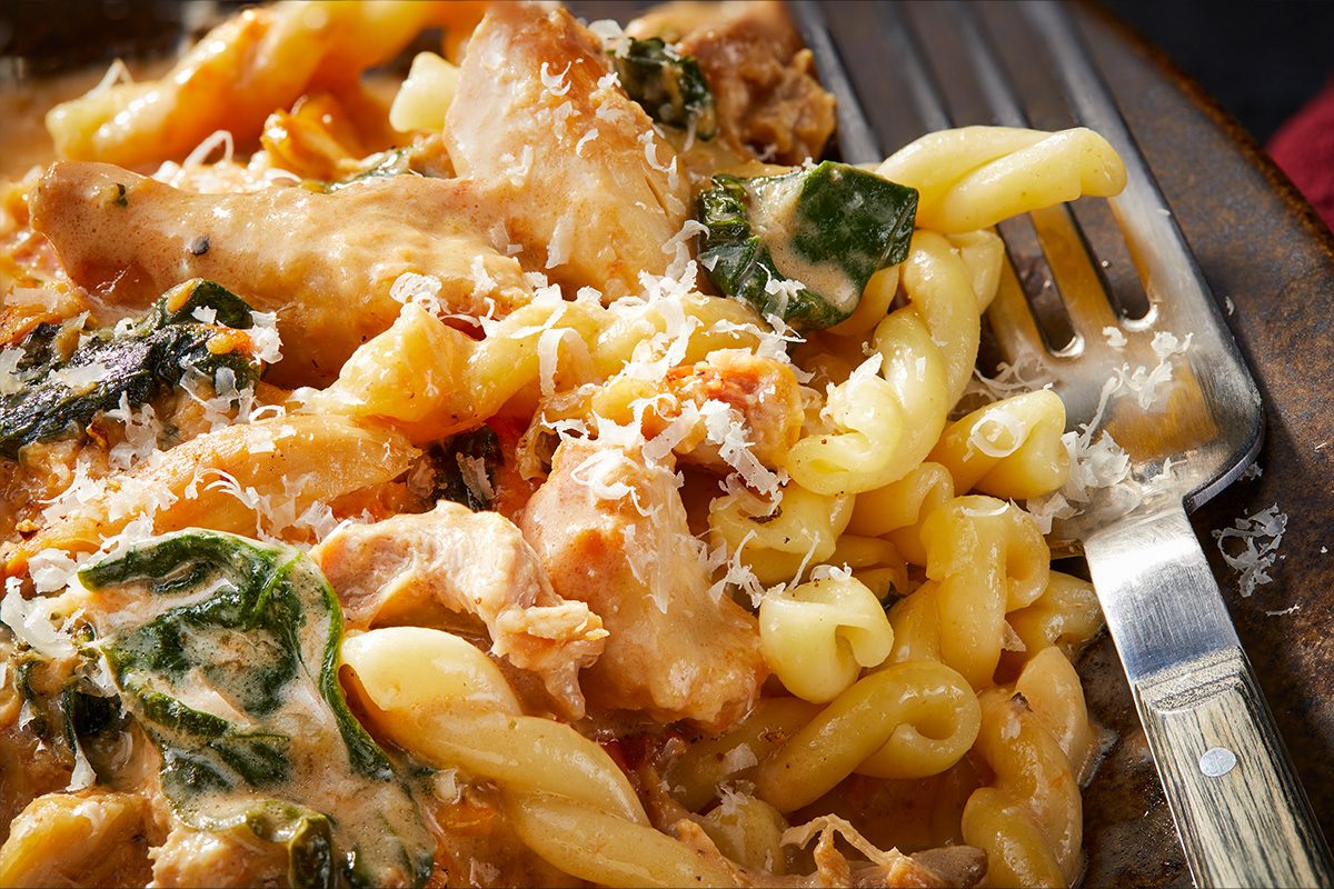 Overhead horizontal close-up of chicken Parma rosa showing creamy sauce, pasta, spinach, and grated Parmesan texture.