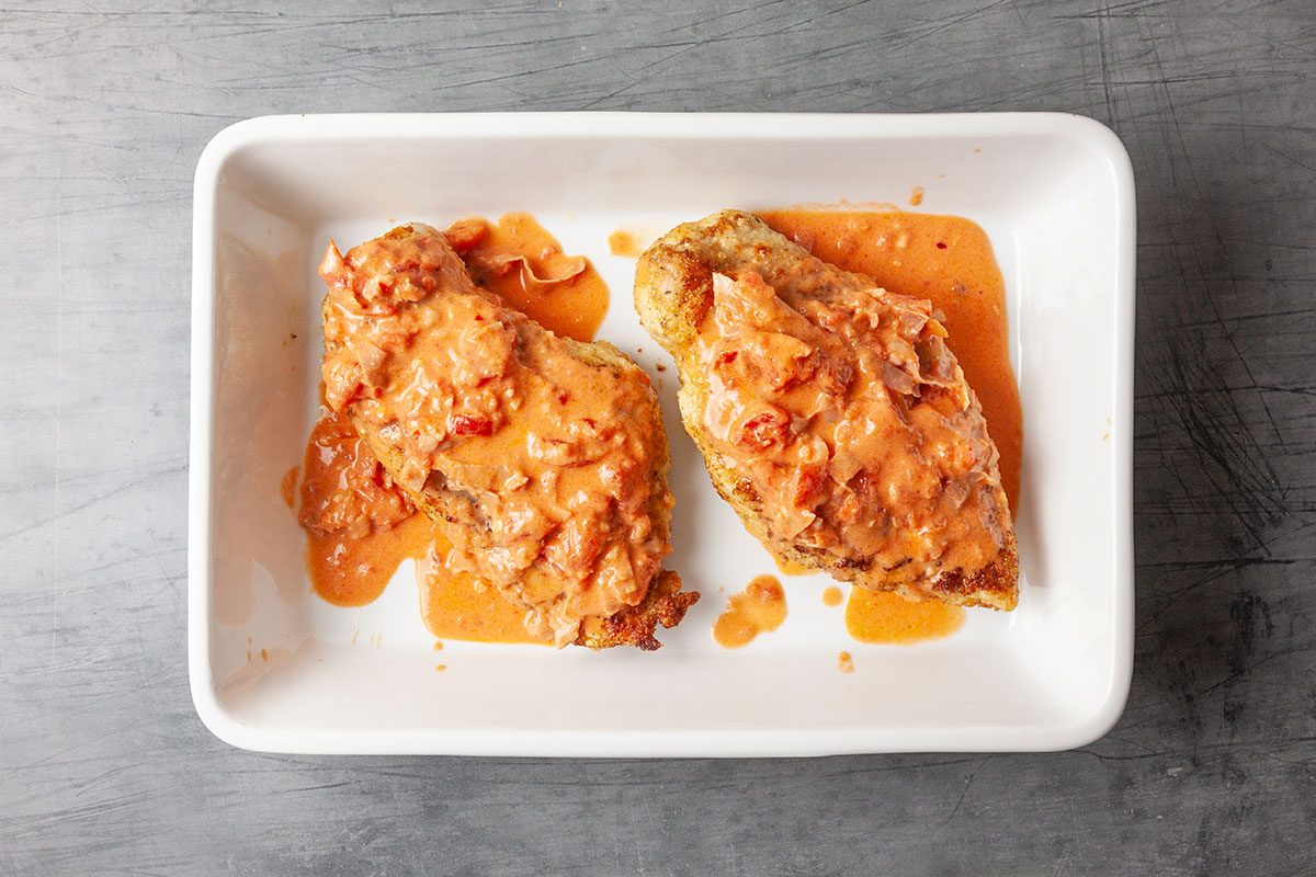 Overhead plating shot of crispy breaded chicken breasts topped with creamy vodka sauce on a white rectangular plate, ready for cheese.