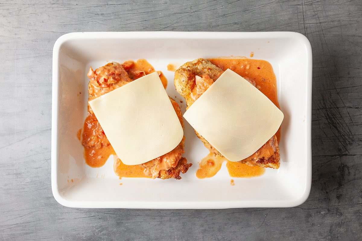 Overhead image of breaded chicken topped with vodka sauce and slices of mozzarella cheese before baking or melting, completing the classic Chicken Parmesan preparation.
