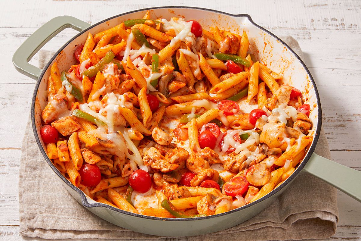 Closeup shot of Italian chicken and penne in a skillet with cherry tomatoes, bell peppers, mushrooms, and melted cheese;
