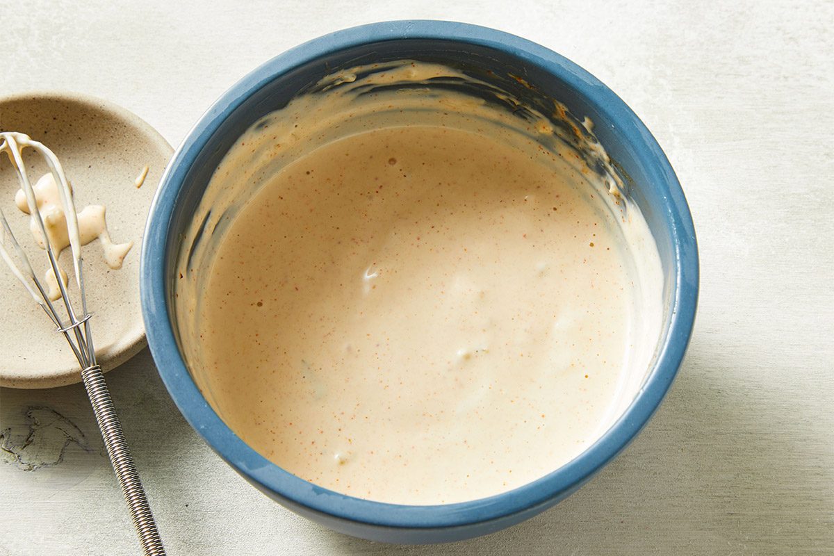 Overhead shot of a blue bowl containing creamy sauce base being whisked for sandwich dressing.