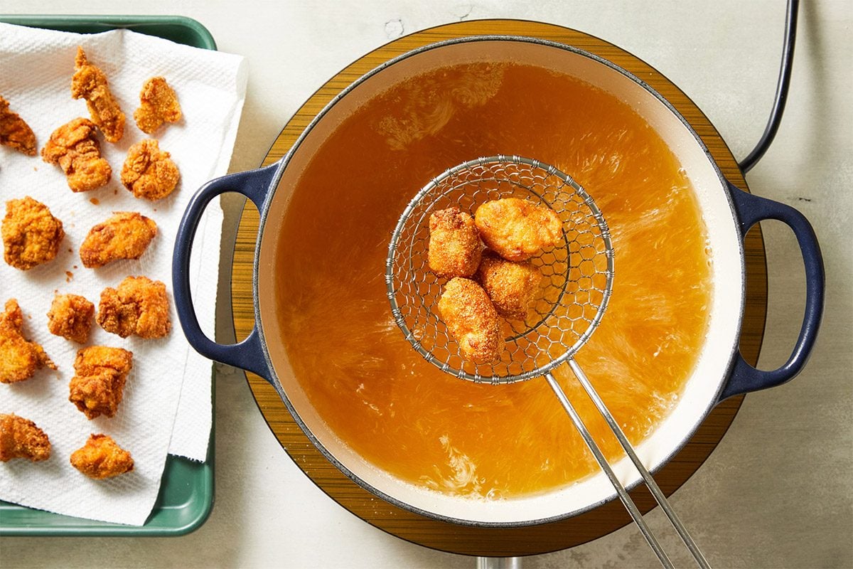 Overhead shot of golden-brown fried chicken bites being lifted from hot oil using a wire skimmer in a pot.