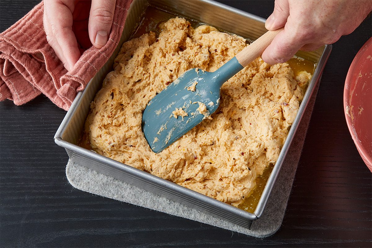 Overhead image of biscuit dough being spread evenly in a baking pan with a spatula before baking the chili crisp biscuits.