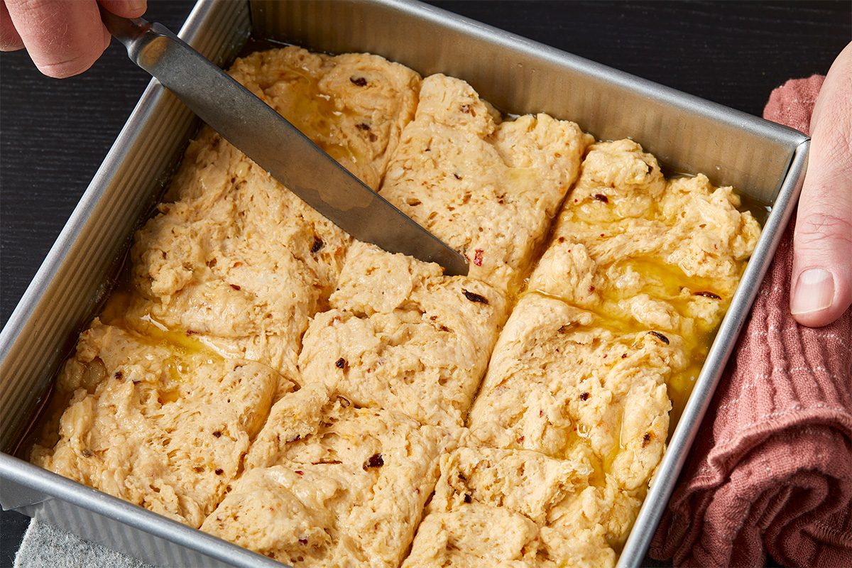 Overhead image of baked biscuit dough being scored with a knife into squares in the baking pan before serving.