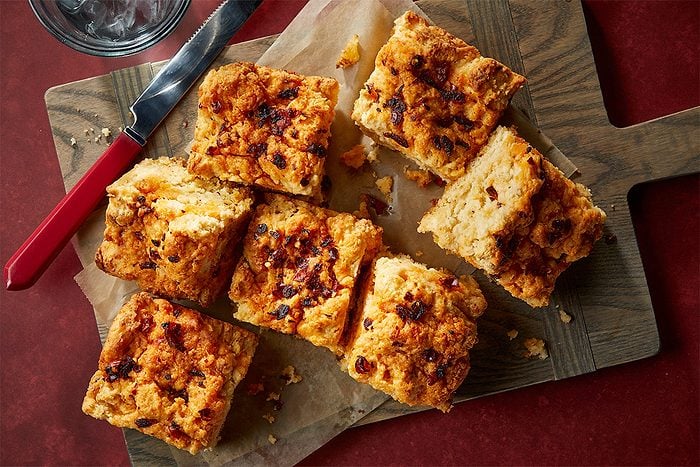 Overhead composition of chili crisp biscuit squares served on a cutting board with a knife, highlighting the golden tops and soft interiors.