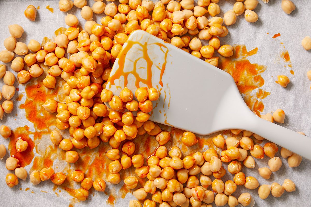 Overhead horizontal image of chickpeas being tossed with chili crisp sauce using a spatula.